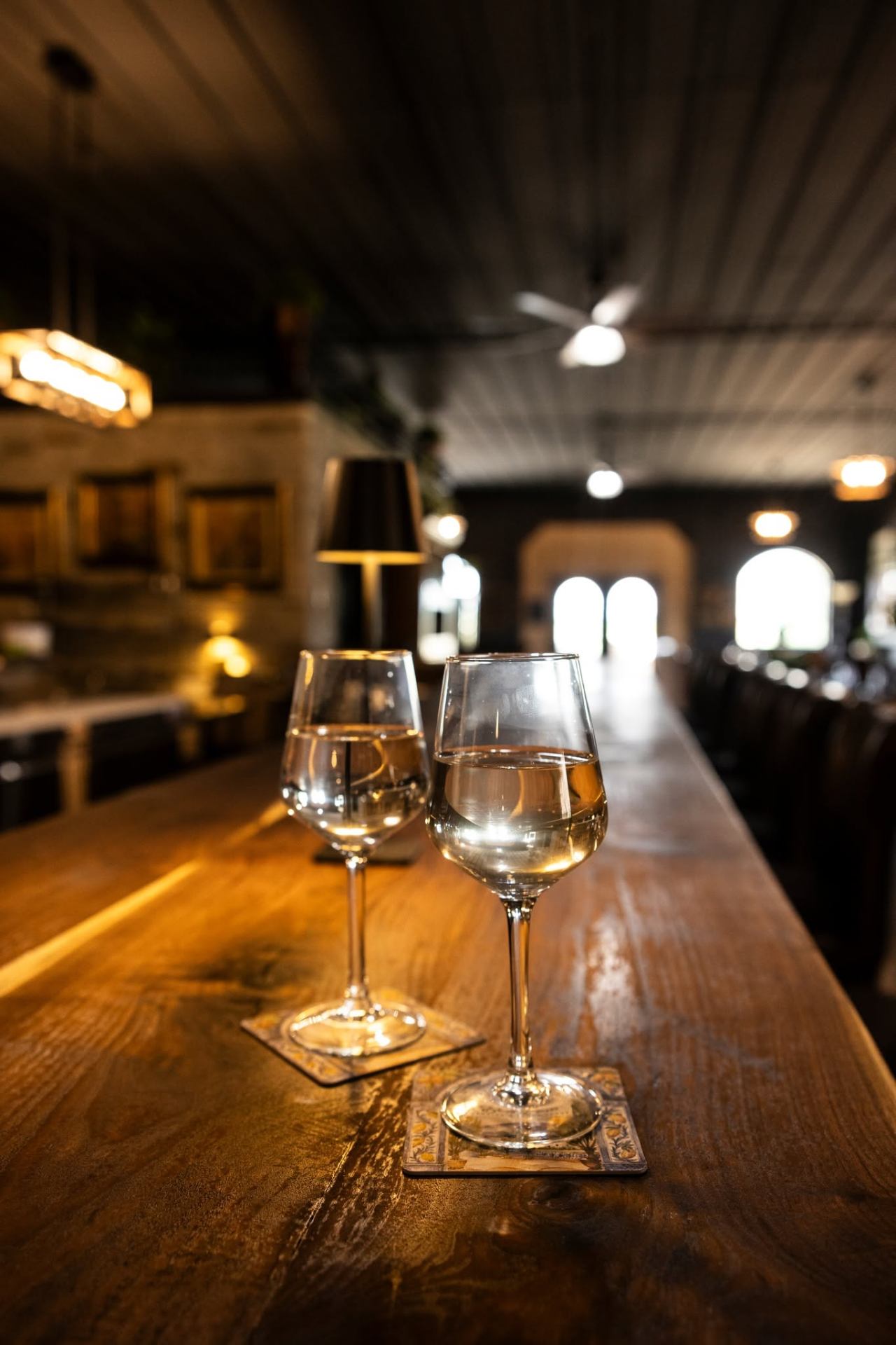 Two wine glasses on a warm wooden bar inside Bella Casa